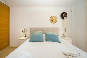 A neatly made bed with a headboard, two bedside tables with lamps, and a wall clock.