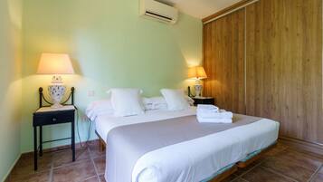 A hotel room with a bed, two bedside tables with lamps, a wall-mounted air conditioner, and a wooden panel wall.