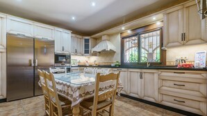 Una cocina con una mesa de comedor, sillas, refrigerador, horno, microondas y armarios.