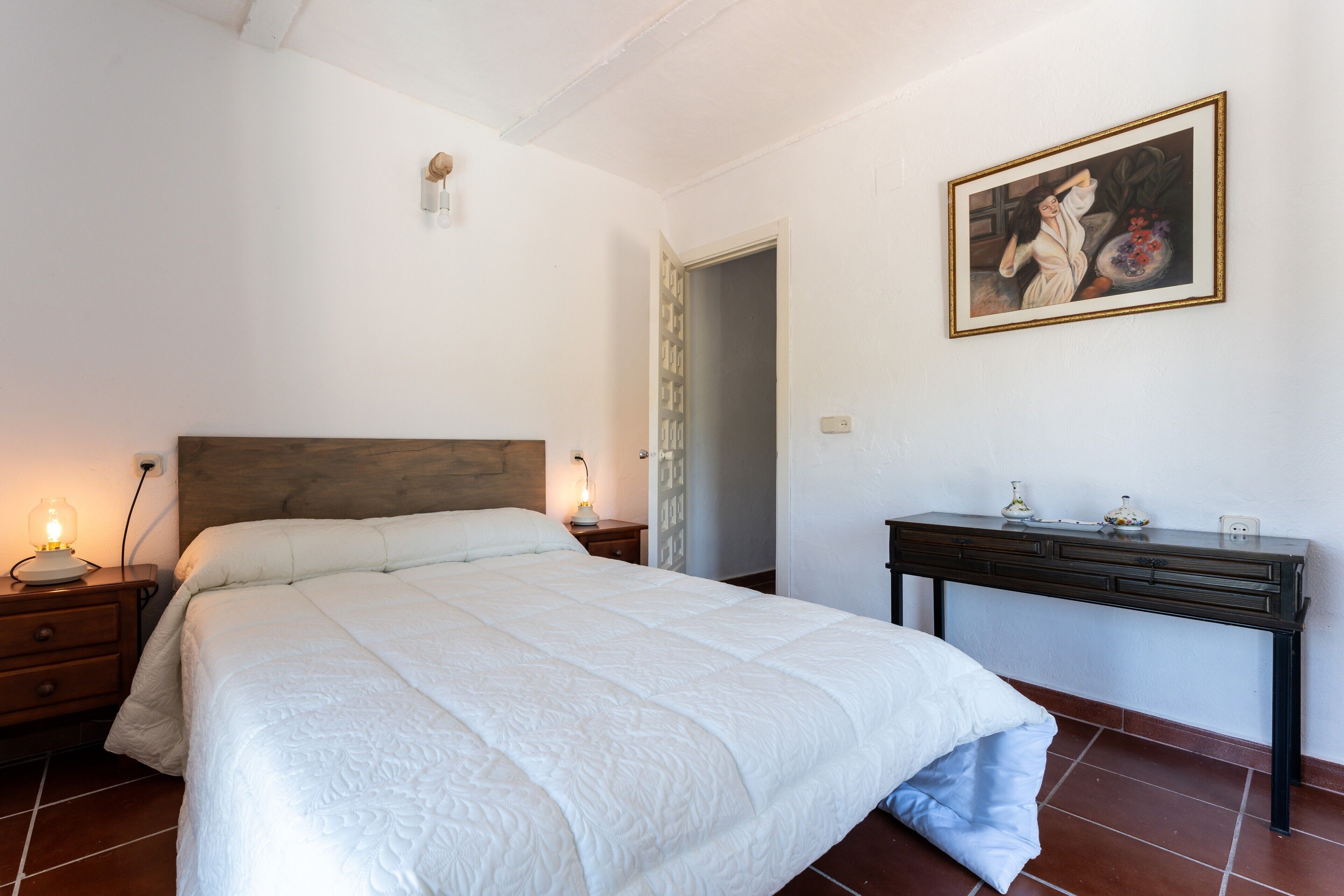 Une chambre à coucher avec un lit, des tables de chevet, un bureau et un tableau accroché au mur.