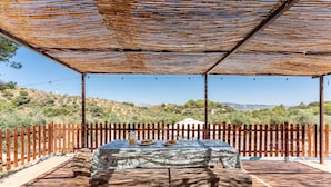 Une terrasse extérieure avec une table et des bancs, entourée d’une clôture en bois et dotée d’un espace ombragé.