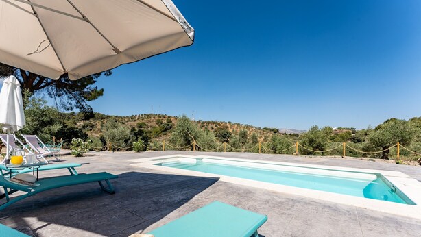 Un espace aménagé au bord de la piscine, avec des chaises longues, un chapeau et une table sur laquelle se trouve une boisson.