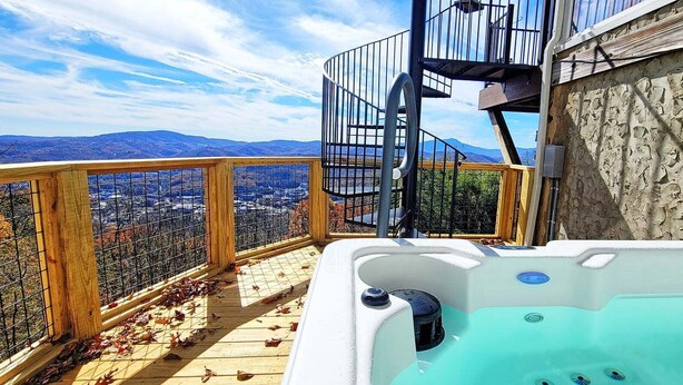 Un jacuzzi en una terraza de madera con vistas a la ciudad, una escalera de caracol y una pared de piedra.