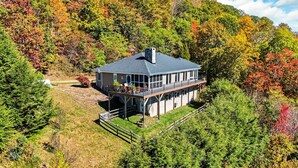 Una casa de dos pisos con un balcón, rodeada por un bosque frondoso.