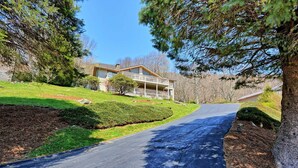 A residential driveway leading to a house with a porch, surrounded by trees and a well-maintained lawn. - Stunning 3BR chalet in Seven Devils, NC, featuring mountain views and a hot tub. (Seven Devils)