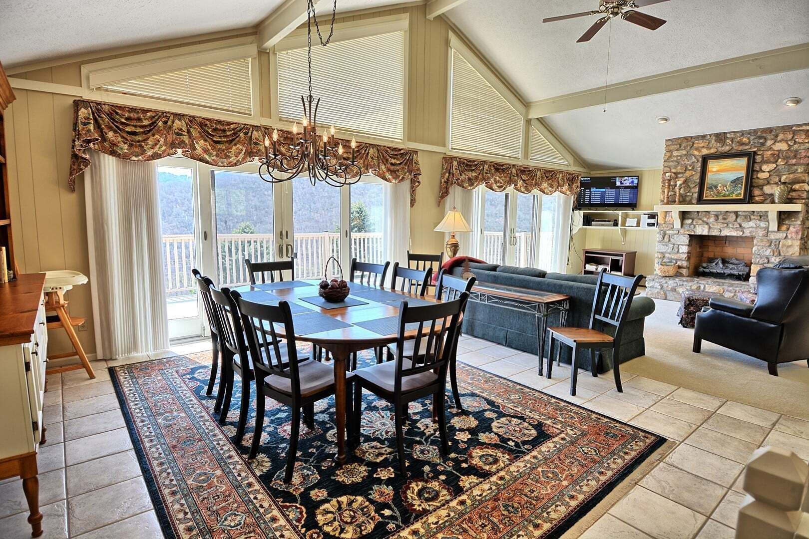 A spacious living room with a fireplace, a dining area with a chandelier, and a balcony with large windows.
