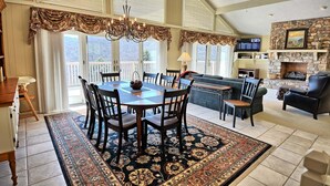 A spacious living room with a fireplace, a dining area with a chandelier, and a balcony with large windows. - Stunning 3BR chalet in Seven Devils, NC, featuring mountain views and a hot tub. (Seven Devils)
