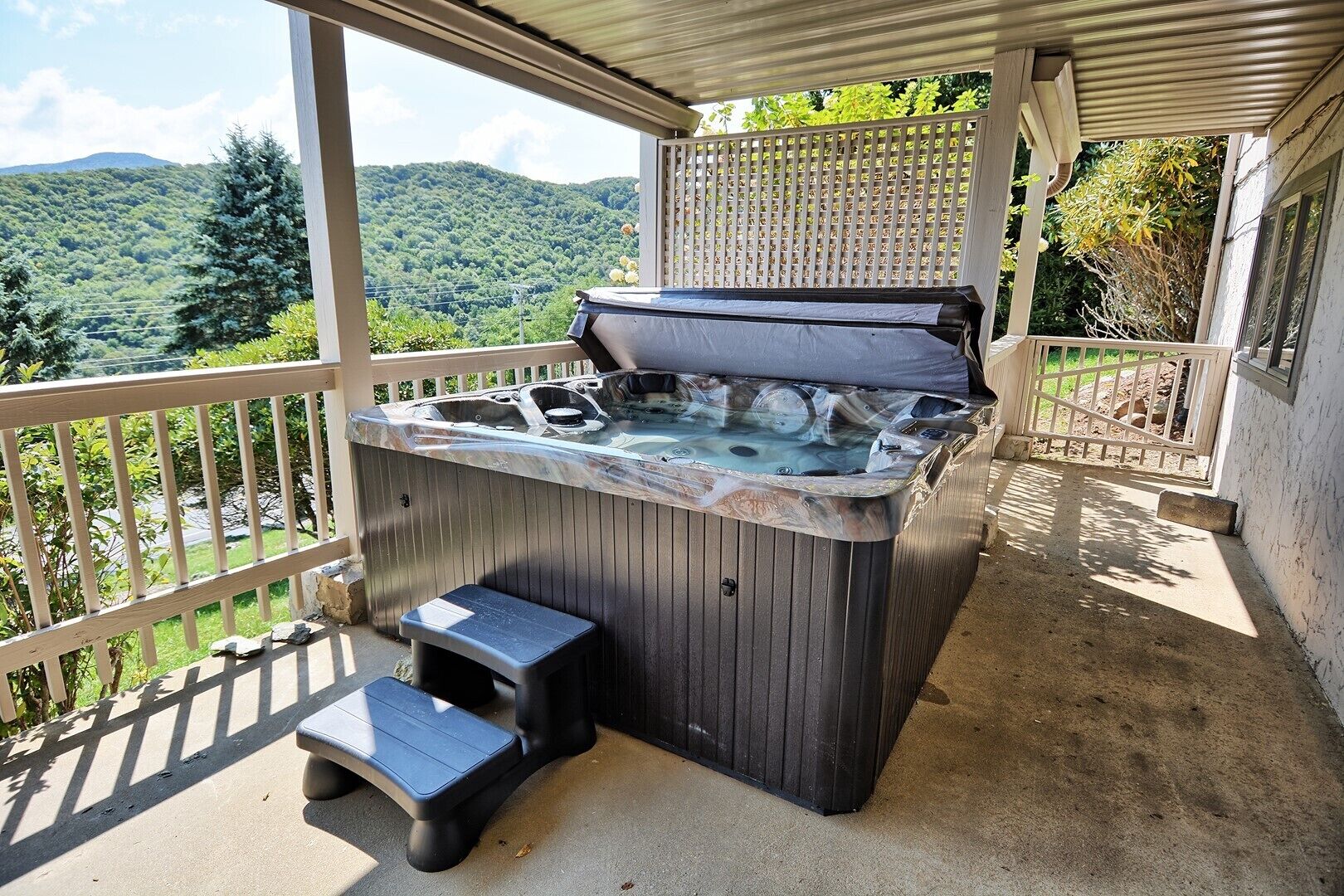 Un bain à remous avec des marches, un patio couvert et une vue sur un paysage montagneux.