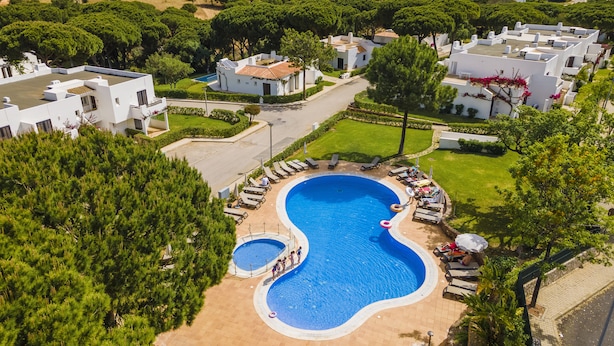 A large swimming pool surrounded by lounge chairs and umbrellas, with a view of a residential area in the background. - Albufeira Family Holidays at Balaia 143 (Albufeira)