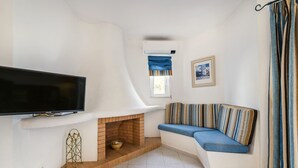A modern living room with a flat-screen TV, a brick fireplace, a blue sofa, and a window with blue curtains. - Albufeira Family Holidays at Balaia 143 (Albufeira)