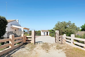 A gated entrance to a property with a gravel driveway leading to a building with a tiled roof.
