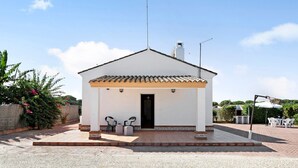 Un pequeño edificio blanco con techo de tejas, una puerta y dos sillas afuera.