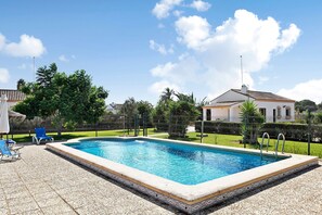 Une piscine rectangulaire bordée de carreaux, entourée d’une clôture, et quelques chaises longues.