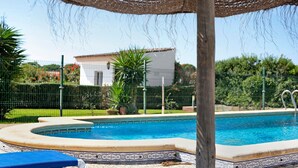 Una piscina con borde de azulejos, una silla de descanso y una pérgola en lo alto.
