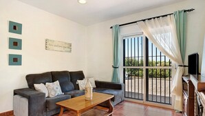 Un salón con sofá, mesa de centro, televisor y puerta corrediza de vidrio a un espacio exterior.
