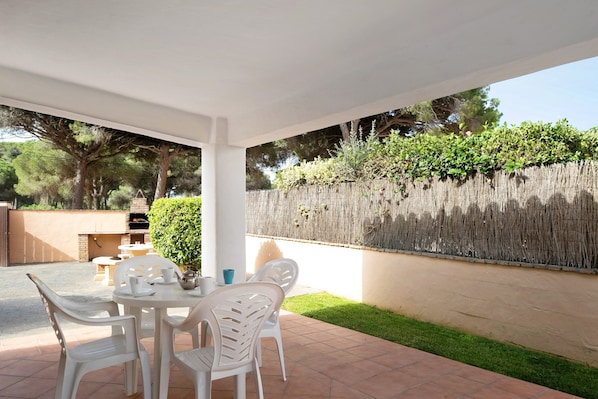 Une terrasse extérieure avec une table et des chaises, un barbecue et une haie.
