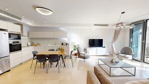 Una cucina moderna con mobili bianchi, un'area pranzo con tavolo e sedie in legno, una TV a schermo piatto e un balcone con vista.