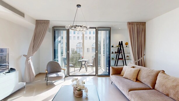 Un soggiorno moderno con un divano, una poltrona, un tavolino da caffè e un balcone vista edifici.