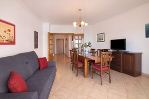 Un salón con sofá, mesa de comedor, sillas, televisión y zona de cocina.