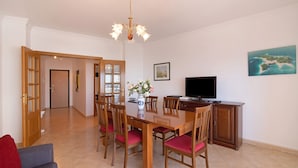A dining area with a wooden table, chairs, a chandelier, a television, and a painting on the wall. - Apartment 'Quarteira Beach Iii' with Balcony, Wi-Fi and Air Conditioning (Quarteira)