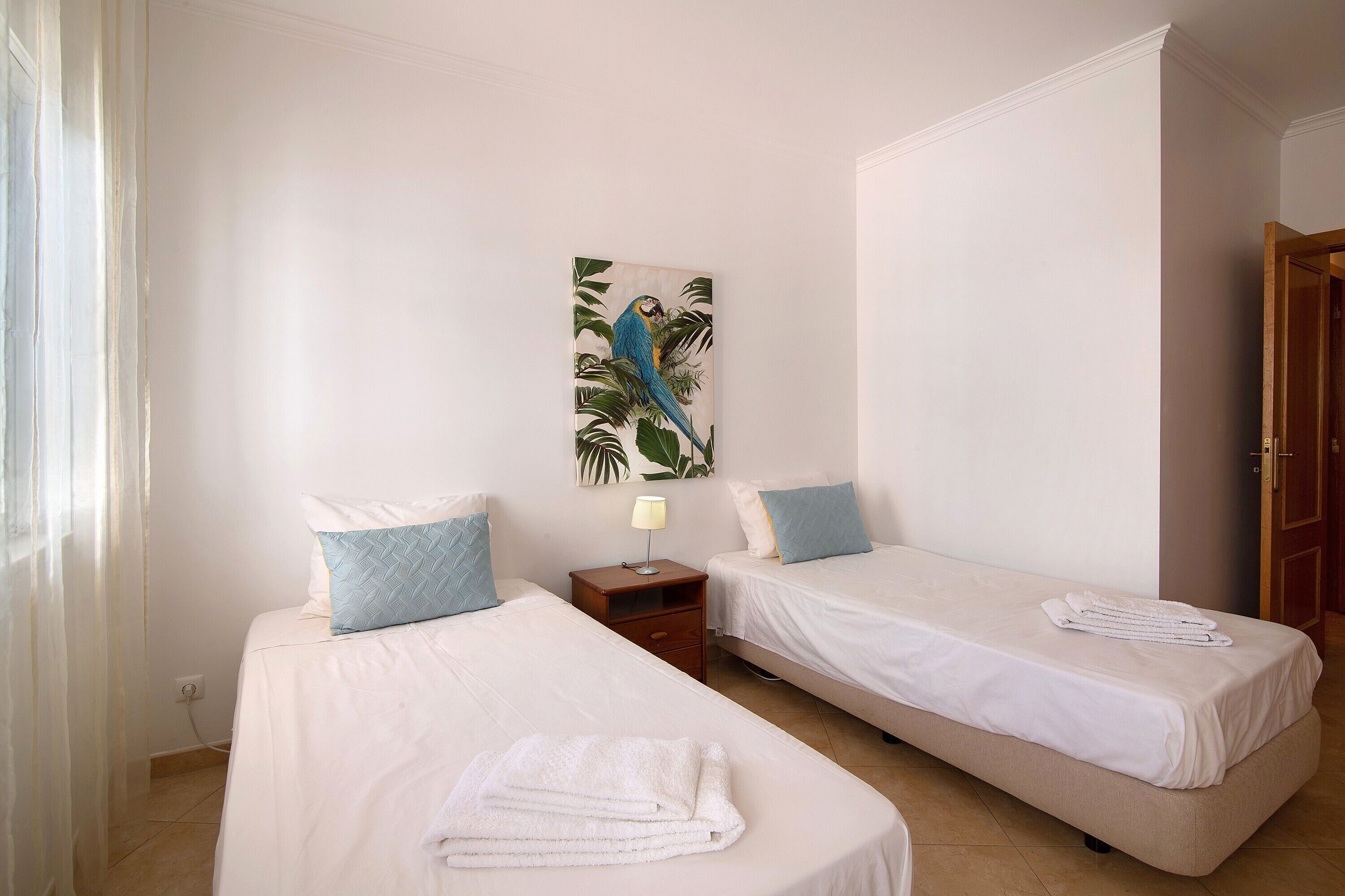 Una habitación con dos camas, una mesita de noche, una lámpara y un cuadro de un pájaro.