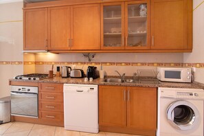 Una cocina con armarios de madera, estufa, lavavajillas, lavadora, microondas y pileta.