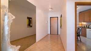 A hallway with a white wall, a door, and a view into a kitchen area. - Apartment 'Quarteira Beach Iii' with Balcony, Wi-Fi and Air Conditioning (Quarteira)
