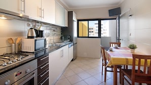 A modern kitchen with stainless steel appliances, a dining area with a table and chairs, and a view through a window. - Apartment 'Quarteira Beach I' with Balcony, Wi-Fi and Air Conditioning (Quarteira)