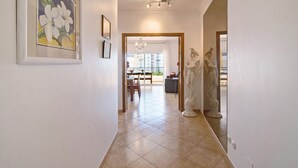 A hallway with a dining area, a chandelier, and a statue. - Apartment 'Quarteira Beach Ii' with Balcony, Wi-Fi and Air Conditioning (Quarteira)