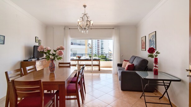 A dining area with a table, chairs, and a vase of flowers. - Apartment 'Quarteira Beach Ii' with Balcony, Wi-Fi and Air Conditioning (Quarteira)