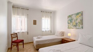 A room with two beds, a chair, a nightstand, and a wall-mounted lamp. - Apartment 'Quarteira Beach Ii' with Balcony, Wi-Fi and Air Conditioning (Quarteira)