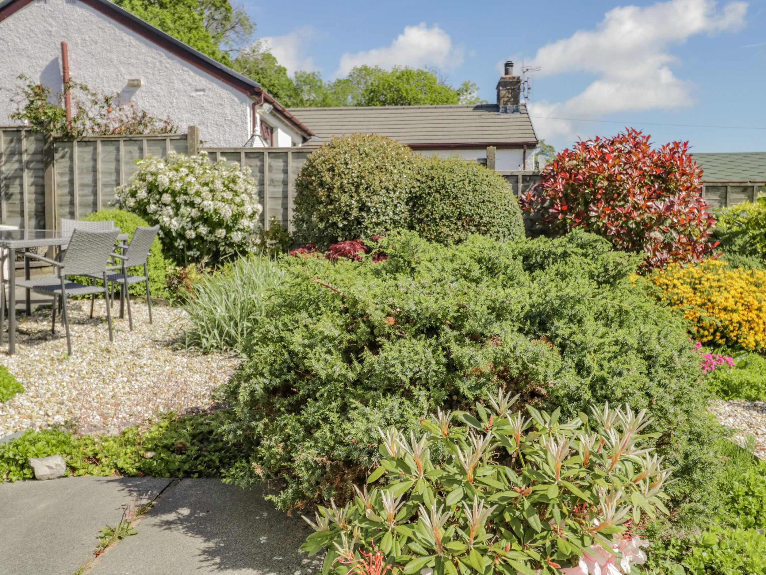 Un jardin avec différentes espèces de plantes et un espace patio aménagé avec des chaises.