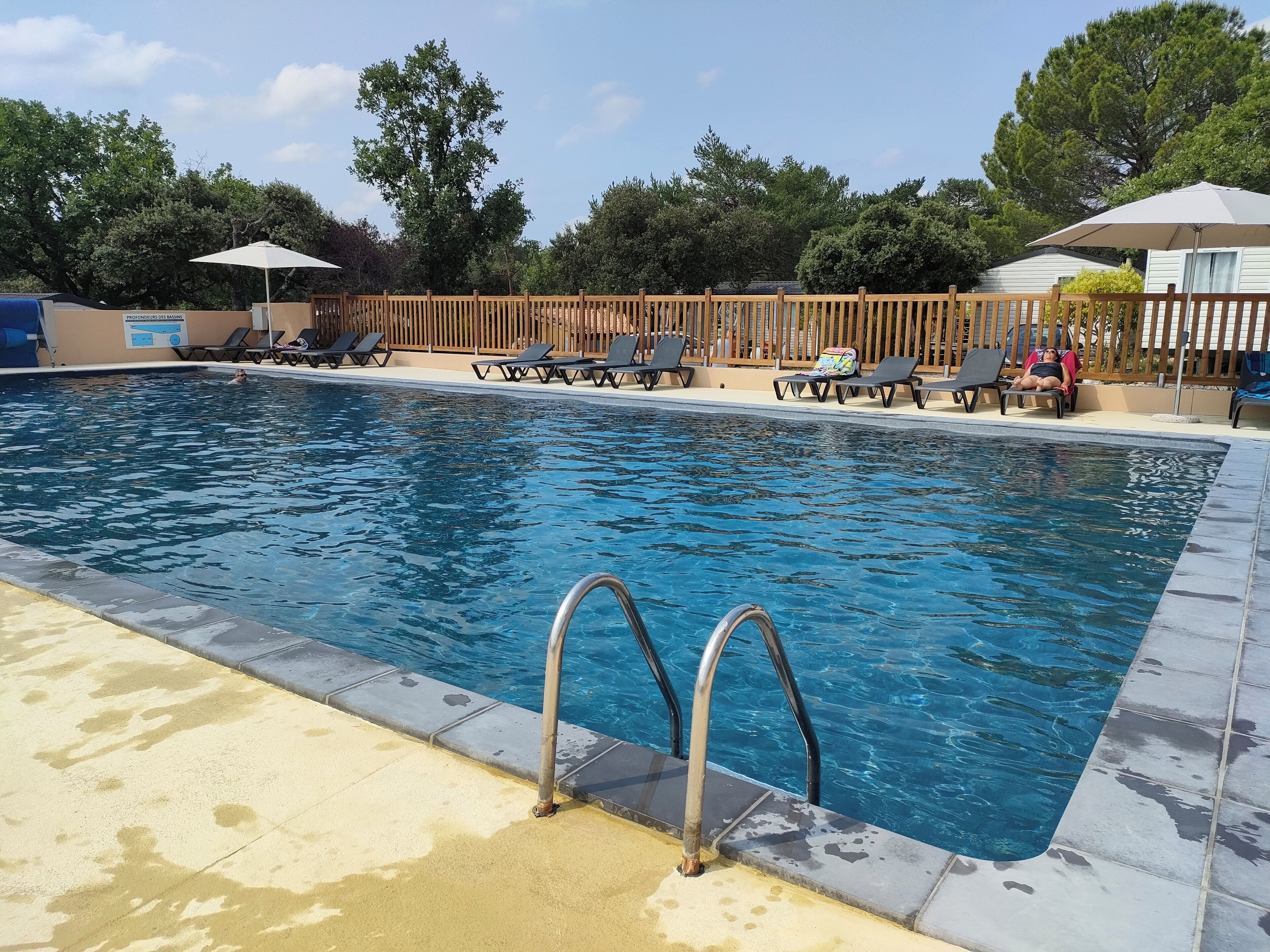 Une piscine rectangulaire dotée d’une terrasse en bois et de chaises longues.