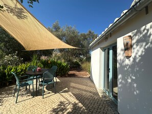 A patio with a table and chairs, a shade sail, and a building with a door. - Holiday Home 'Casa Cobra' with Mountain View, Shared Pool, Garden & Wi-Fi (Moncarapacho)