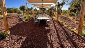 A covered outdoor dining area with a table set for multiple people, surrounded by a garden with various plants and trees. - Holiday Home 'Casa Cobra' with Mountain View, Shared Pool, Garden & Wi-Fi (Moncarapacho)