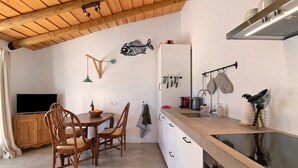A compact kitchen with a wooden ceiling, a dining area with a table and chairs, and a TV on the left. - Holiday Home 'Casa Cobra' with Mountain View, Shared Pool, Garden & Wi-Fi (Moncarapacho)