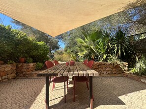 An outdoor patio with a wooden table and red chairs, surrounded by stone walls and various plants. - Holiday Home 'Casa Frango' with Mountain View, Shared Pool, Garden & Wi-Fi (Moncarapacho)