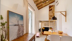 A dining area with a wooden table, white chairs, a small pink stool, a wooden bench, and a painting of a lighthouse. - Holiday Home Casa Burro with Mountain View, Shared Pool, Garden & Wi-Fi (Moncarapacho)