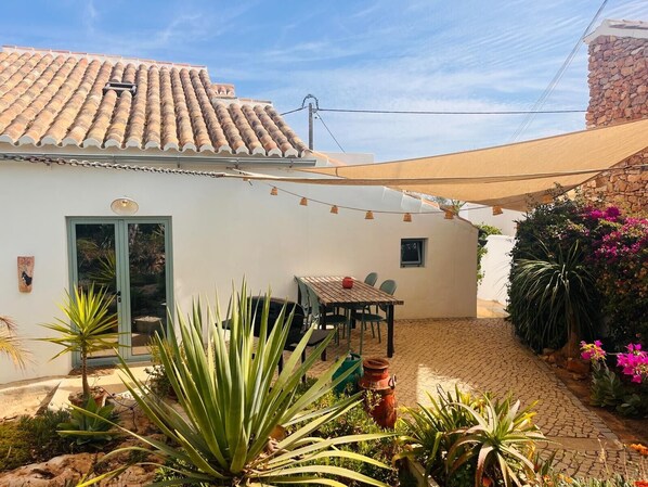 Ein Haus mit Ziegeldach, einer Terrasse mit Tisch und Stühlen sowie ein Garten mit verschiedenen Pflanzen.