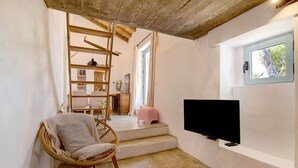 A room with a television, a wicker chair, a staircase, and a window. - Holiday Home Casa Burro with Mountain View, Shared Pool, Garden & Wi-Fi (Moncarapacho)