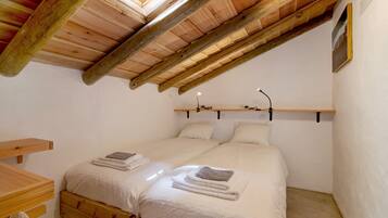 Une chambre avec un plafond en bois, deux lits, une table de chevet et une étagère fixée au mur.