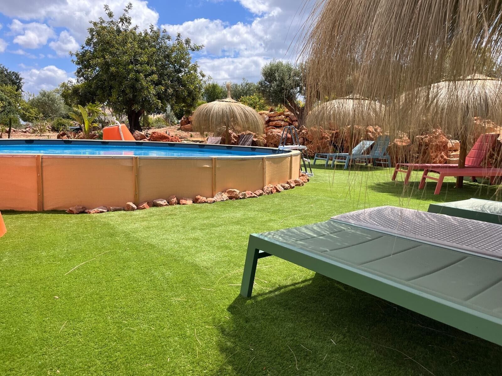 Ein Garten mit Schwimmbad, Kunstgrasanlage, Liegestühlen und einem Steingarten.