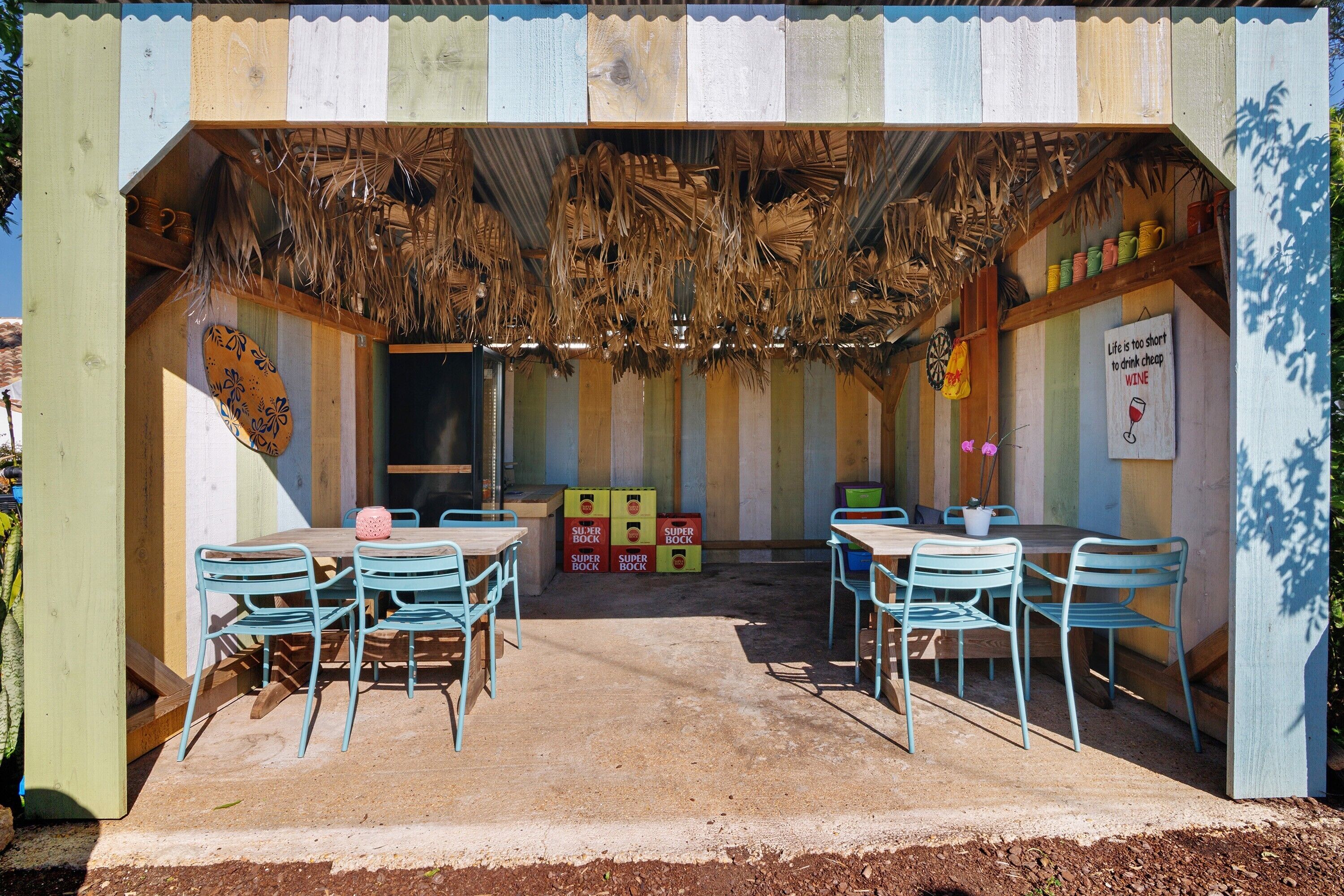 Un espacio de estar al aire libre rústico con mesas y sillas de madera, techo de paja y cajas de almacenamiento coloridas.