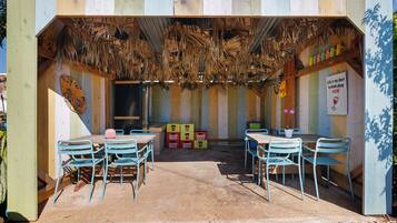 Un espacio de estar al aire libre rústico con mesas y sillas de madera, techo de paja y cajas de almacenamiento coloridas.