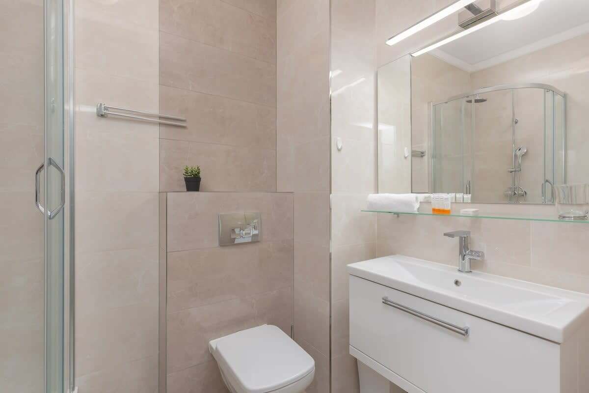 Un baño moderno con cabina de ducha de vidrio, inodoro blanco y tocador con espejo.