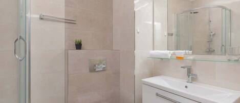 Un baño moderno con cabina de ducha de vidrio, inodoro blanco y tocador con espejo.
