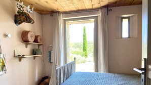Un dormitorio con cama, estanterías de madera, ventana con cortinas y vistas a zonas verdes.