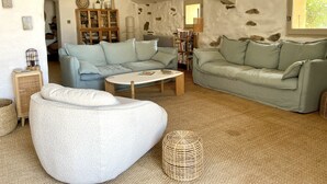 Una sala de estar acogedora con un sofá seccional azul claro, un otoman blanco y una mesa de centro. Se aprecia una estantería llena de libros y objetos decorativos.
