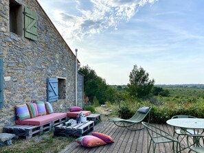 A rustic stone building with a wooden deck, outdoor seating, and a table. - Beautiful stone sheep barn in the garrigue—with all the comforts—La Palme (11) (La Palme)