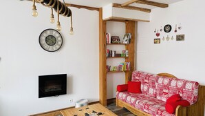 Ein gemütliches Wohnzimmer mit einem Holzsofa, einem Bücherregal, einer Wanduhr und einer Pendelleuchte.